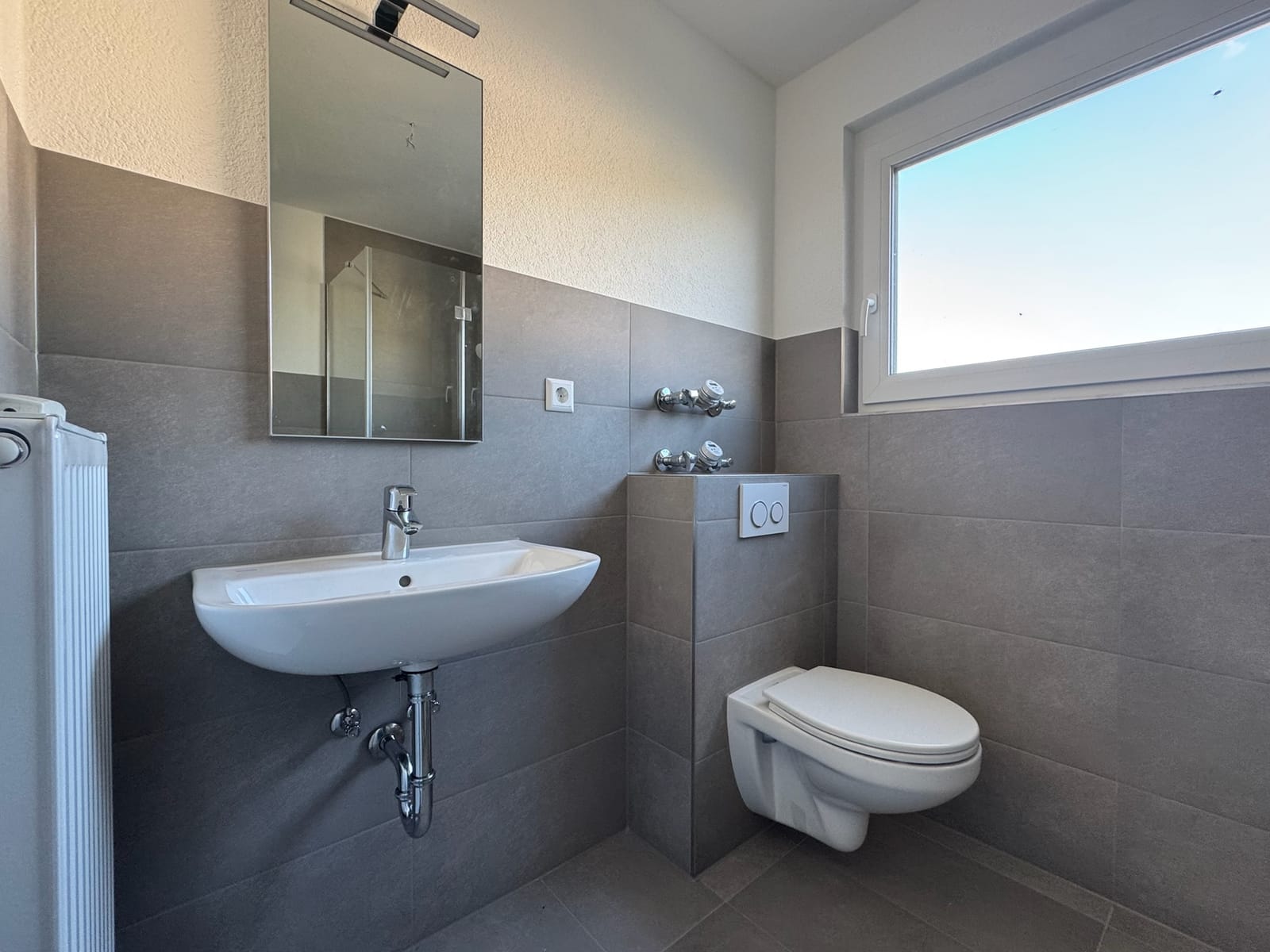 Badezimmer nach der Sanierung mit großformatigen grauen Fliesen und wandhängendem WC